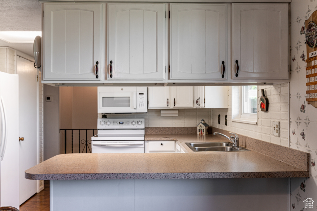 Kitchen with white appliances, a peninsula, tasteful backsplash, white cabinetry, and wood finished floors