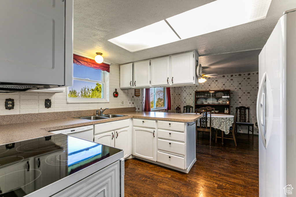 Kitchen featuring white appliances, dark wood-style floors, white cabinetry, a peninsula, and backsplash