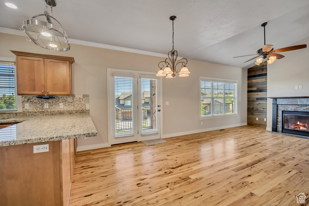 Kitchen featuring light wood-type flooring, open floor plan, a stone fireplace, a ceiling fan, and backsplash