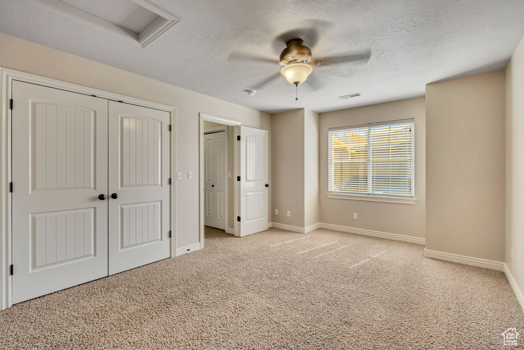 Unfurnished bedroom with light colored carpet, attic access, a textured ceiling, and a ceiling fan
