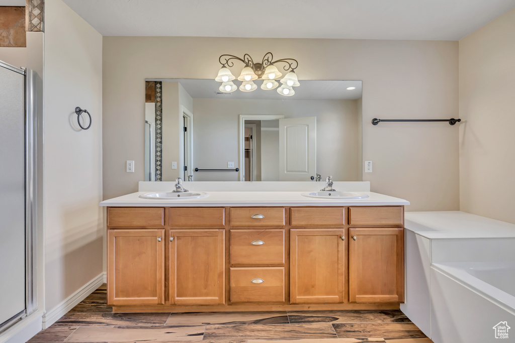 Bathroom featuring wood finished floors, double vanity, a stall shower, a chandelier, and a bath