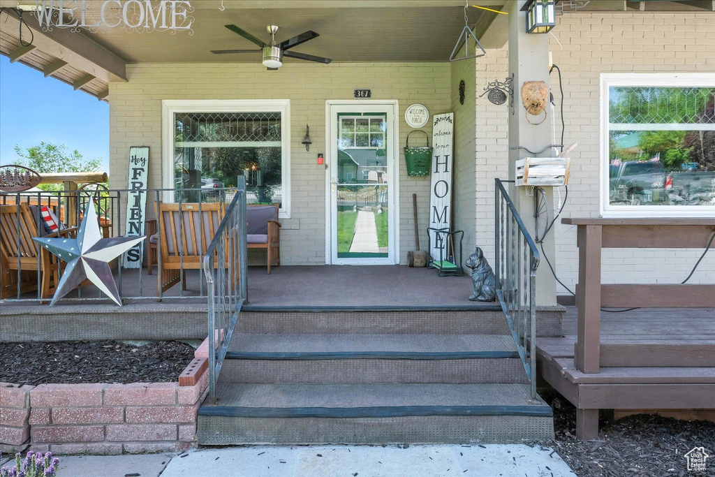 Doorway to property with brick siding, a porch, and ceiling fan