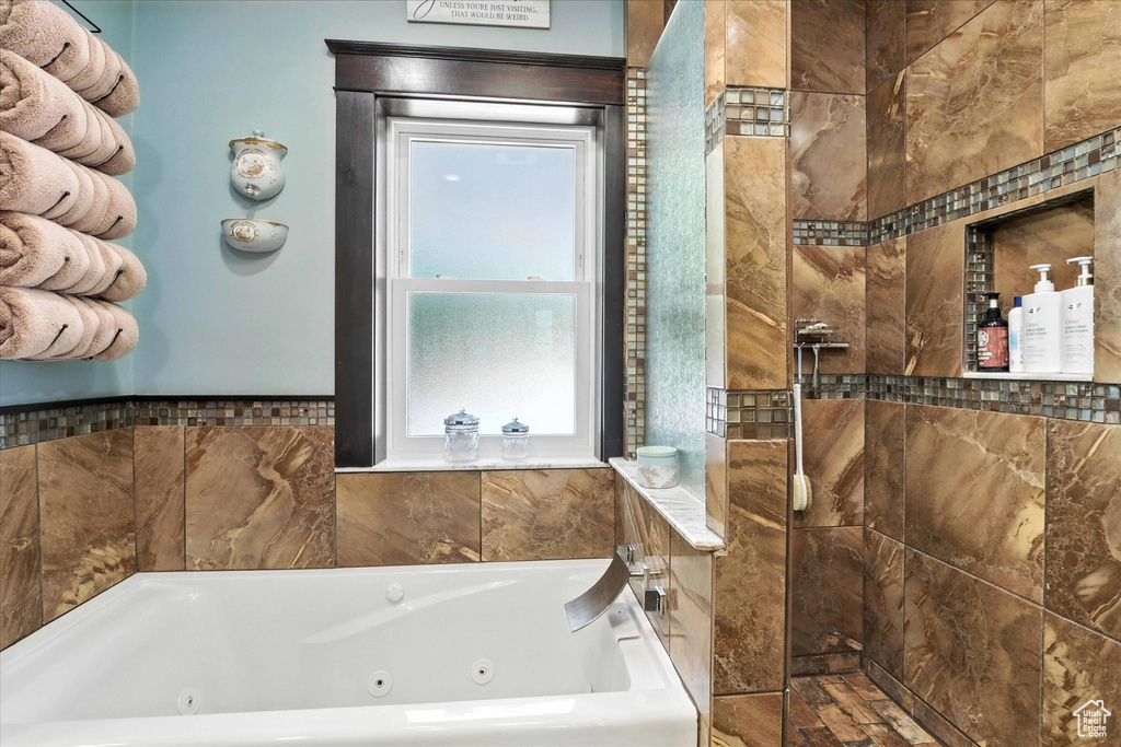 Bathroom with healthy amount of natural light, a whirlpool tub, and a tile shower