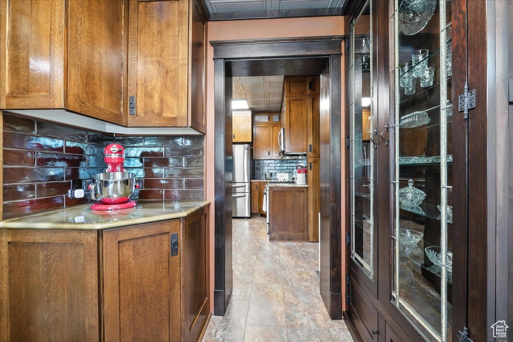 Kitchen with brown cabinets, decorative backsplash, light countertops, and freestanding refrigerator