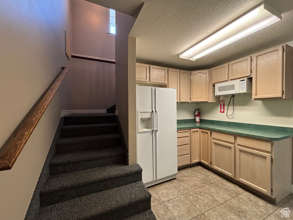 Kitchen featuring white appliances, dark countertops, a textured ceiling, and light tile patterned floors