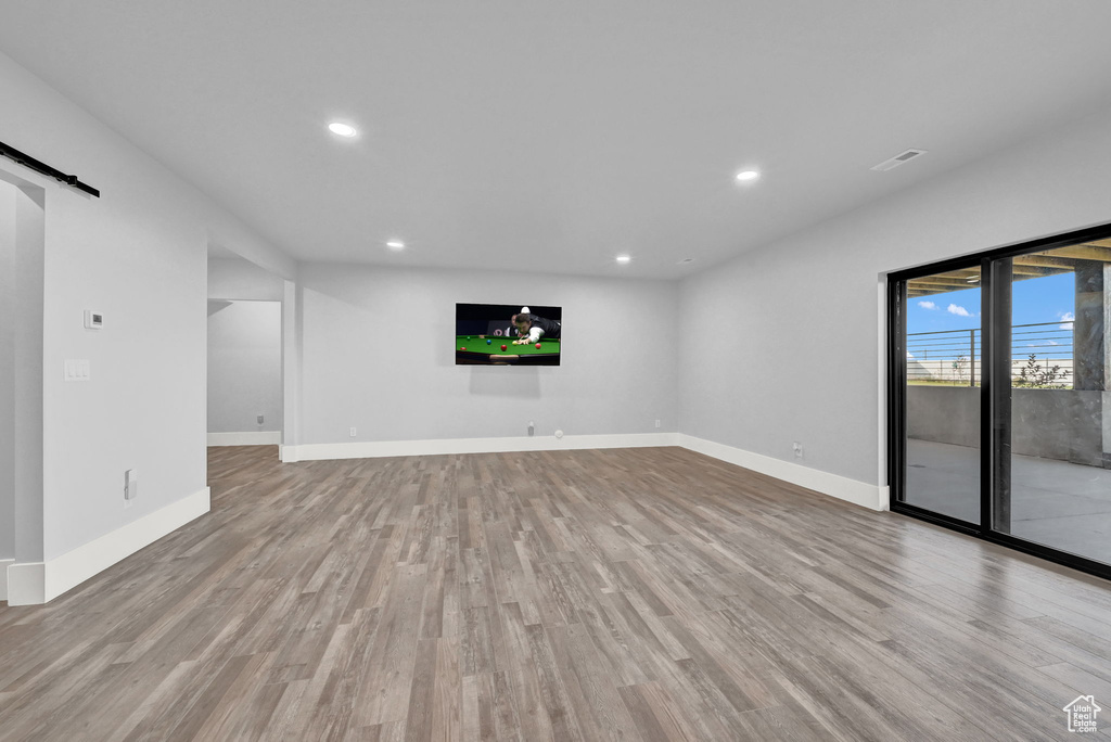 Unfurnished living room with wood finished floors, recessed lighting, and a barn door