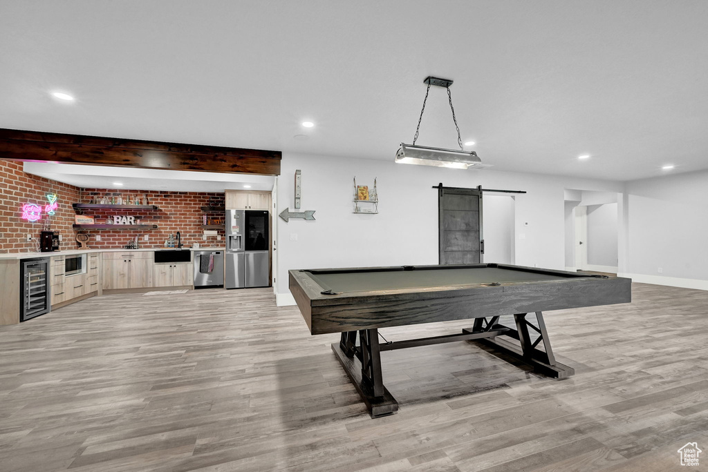 Recreation room featuring beverage cooler, light wood-style floors, a barn door, bar with sink, and recessed lighting