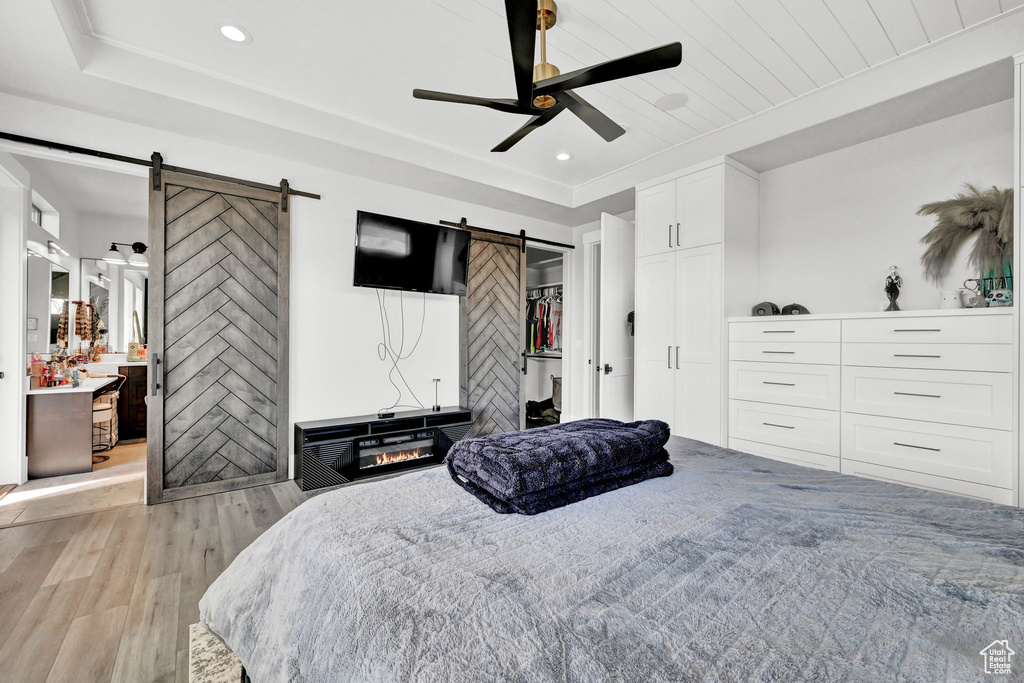 Bedroom with a barn door, light wood-style floors, ceiling fan, and recessed lighting