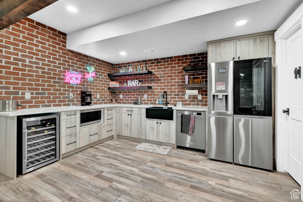 Kitchen with wine cooler, stainless steel appliances, light countertops, light brown cabinets, and brick wall