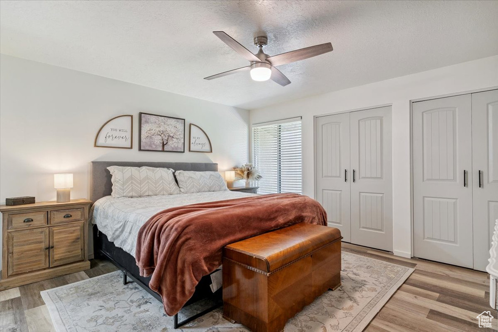 Bedroom featuring light wood-type flooring, multiple closets, a ceiling fan, and a textured ceiling