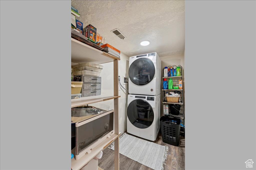 Laundry room featuring estacked washer and dryer, wood finished floors, and a textured ceiling