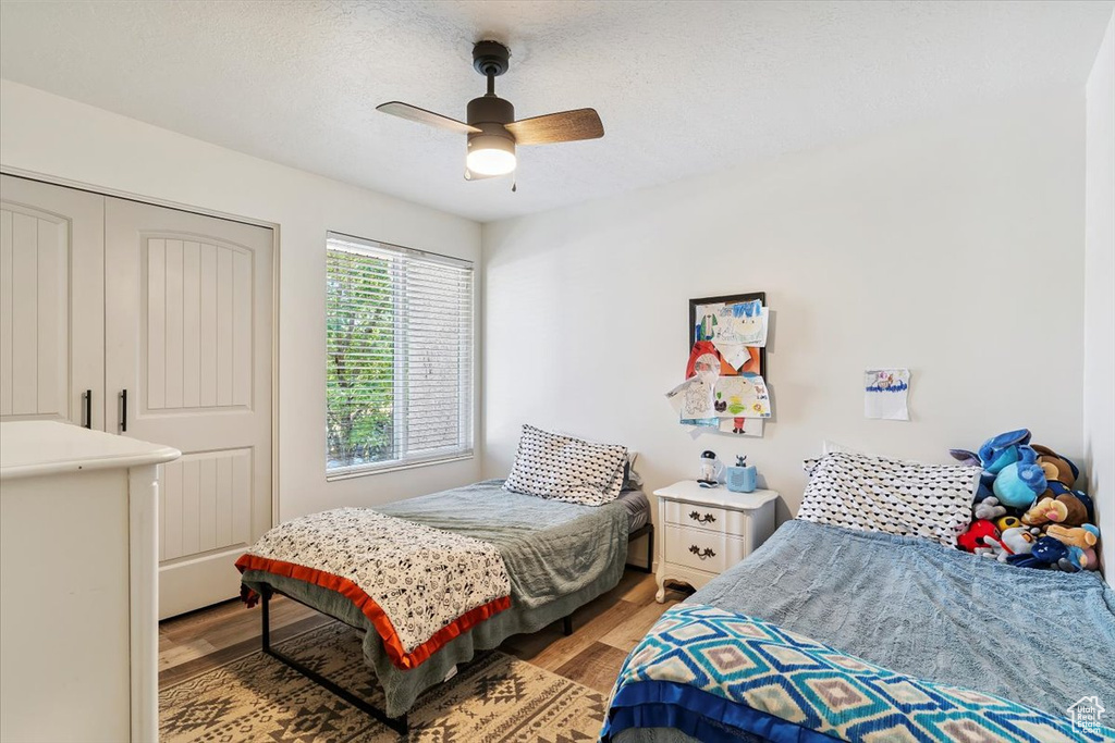 Bedroom with light wood-style flooring, ceiling fan, a closet, and a textured ceiling
