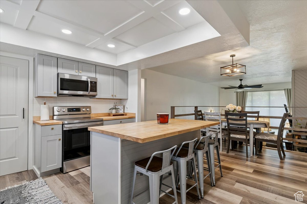 Kitchen with butcher block counters, stainless steel appliances, coffered ceiling, light wood-style flooring, and a ceiling fan