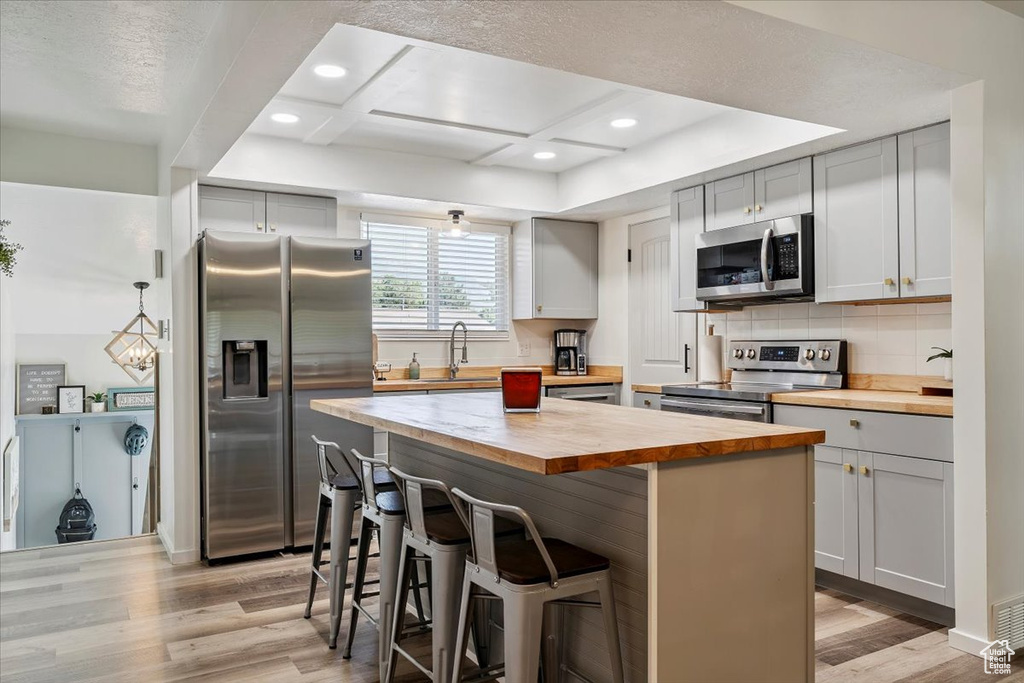 Kitchen featuring butcher block counters, stainless steel appliances, light wood-style flooring, a kitchen bar, and a kitchen island