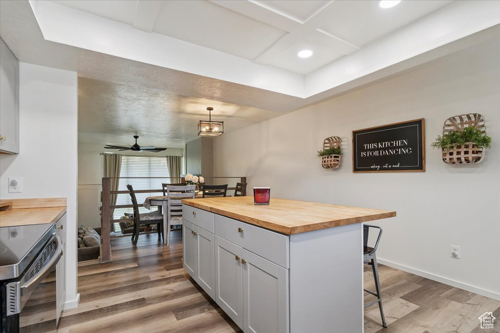 Kitchen with butcher block countertops, electric range, a breakfast bar, light wood-style flooring, and coffered ceiling