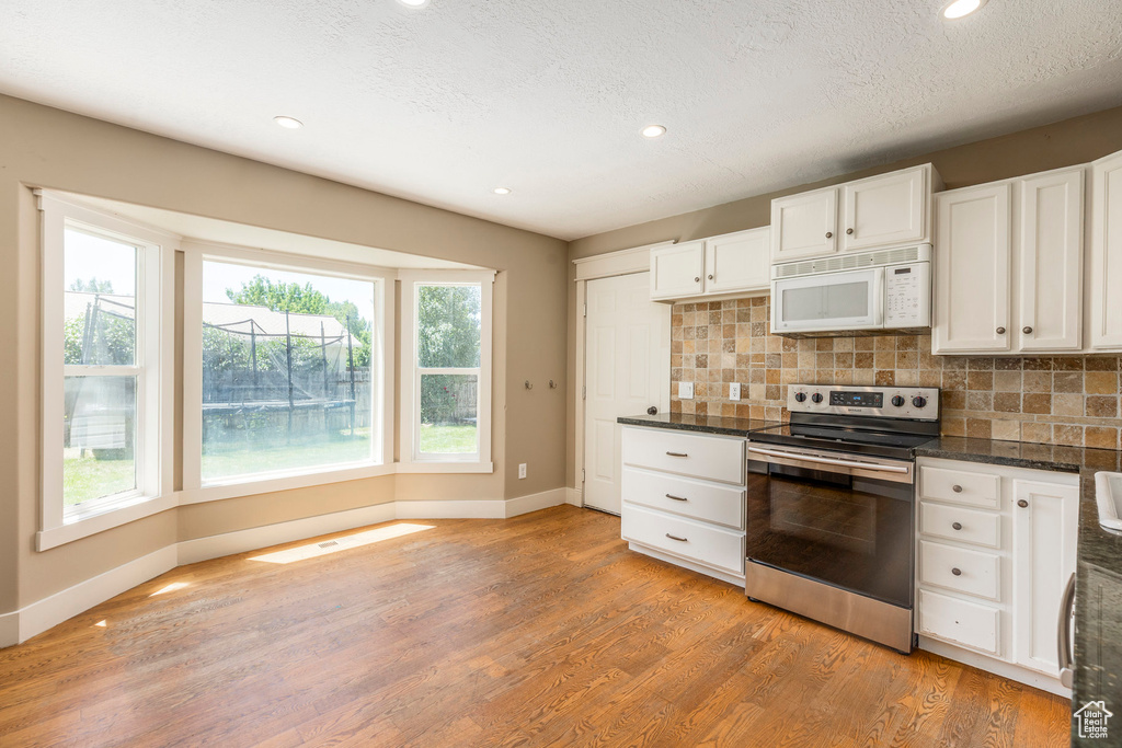 Kitchen with white microwave, stainless steel range with electric cooktop, dark countertops, light wood-style floors, and tasteful backsplash