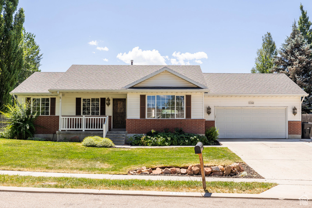 Single story home with a porch, an attached garage, brick siding, and a front yard