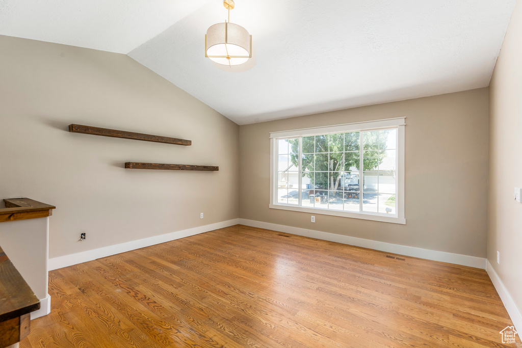 Empty room with light wood finished floors and lofted ceiling