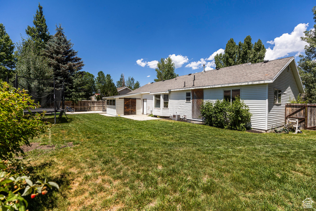 Rear view of house featuring a trampoline, a patio, a fenced backyard, and a shingled roof