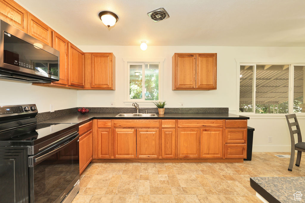 Kitchen featuring black range with electric cooktop, stainless steel microwave, dark countertops, and brown cabinetry