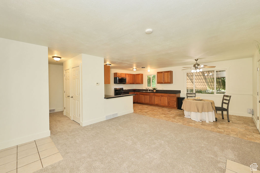 Kitchen with stainless steel microwave, dark countertops, brown cabinetry, range with electric stovetop, and a ceiling fan