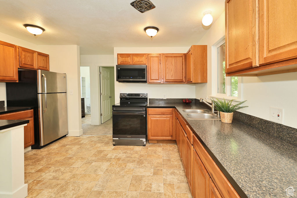 Kitchen with appliances with stainless steel finishes, dark countertops, brown cabinets, and light stone finish floors