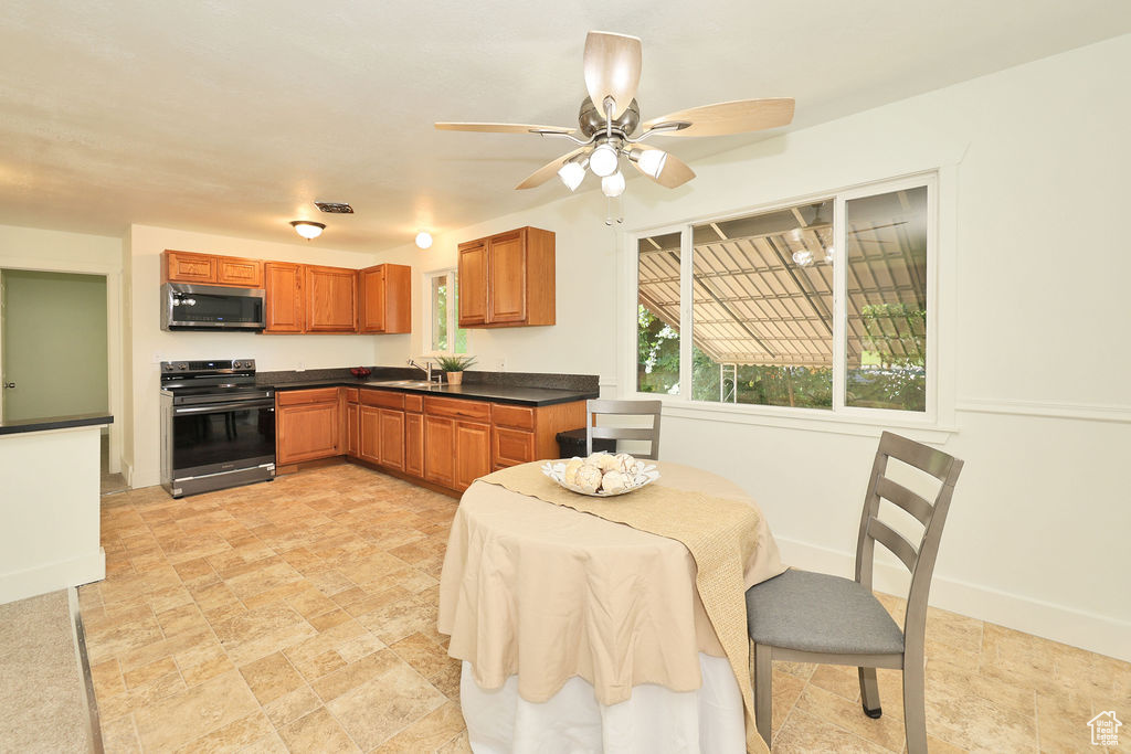 Kitchen featuring stainless steel appliances, dark countertops, brown cabinets, a ceiling fan, and stone finish flooring