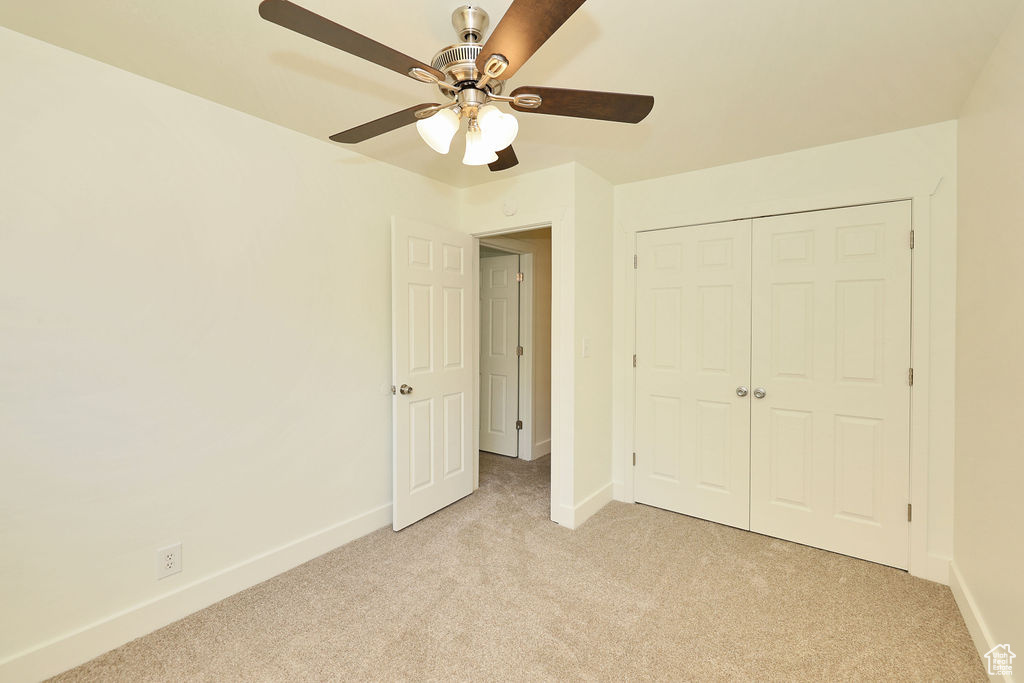 Unfurnished bedroom with light colored carpet, a closet, and a ceiling fan