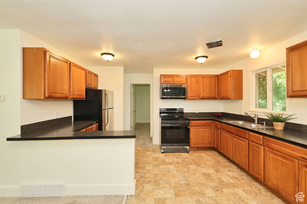Kitchen with appliances with stainless steel finishes, dark countertops, brown cabinetry, and a peninsula