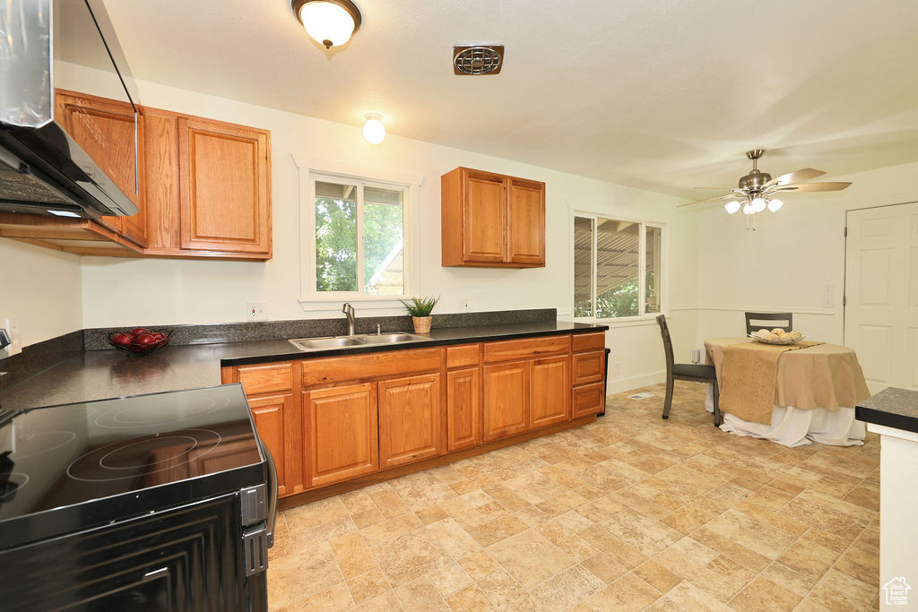 Kitchen with range hood, range with electric cooktop, dark countertops, brown cabinetry, and ceiling fan