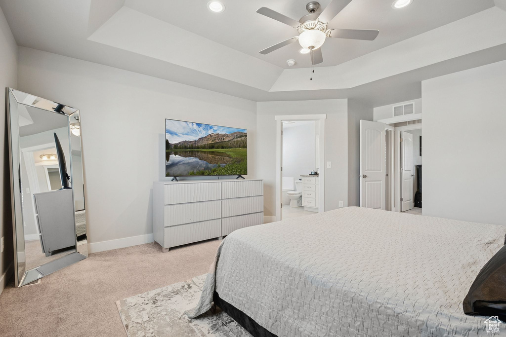 Bedroom with light colored carpet, a raised ceiling, ensuite bathroom, recessed lighting, and a ceiling fan