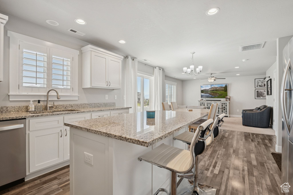 Kitchen featuring stainless steel dishwasher, a chandelier, dark wood finished floors, a kitchen island, and white cabinetry