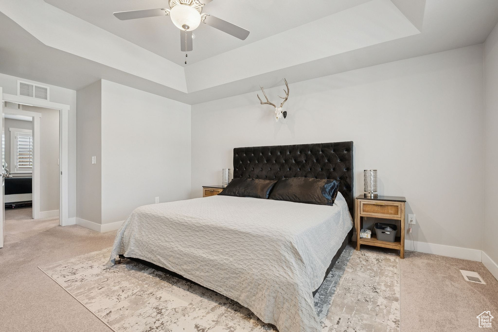 Carpeted bedroom with a raised ceiling and a ceiling fan