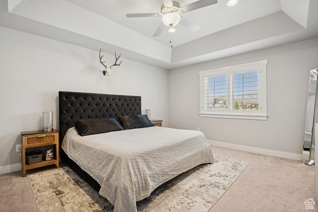 Bedroom featuring a raised ceiling, light colored carpet, and ceiling fan