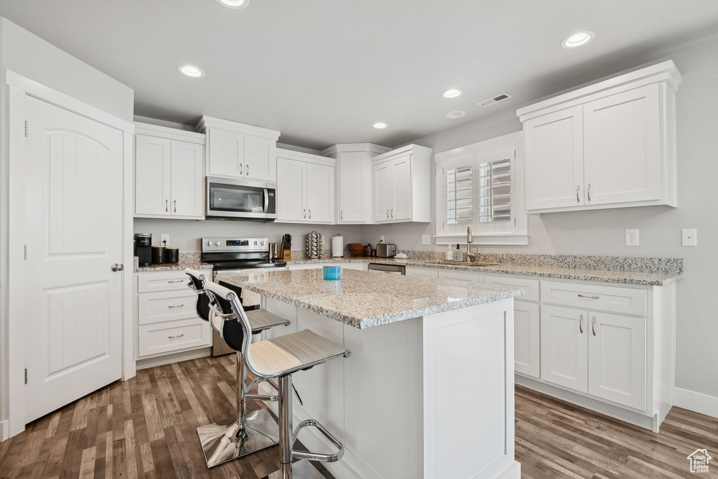 Kitchen with appliances with stainless steel finishes, wood finished floors, white cabinetry, a kitchen island, and a breakfast bar area
