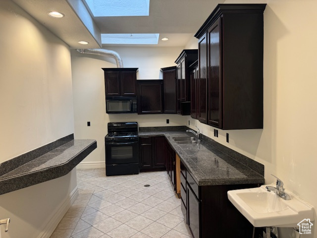 Kitchen with black appliances, a skylight, light tile patterned floors, recessed lighting, and dark cabinets