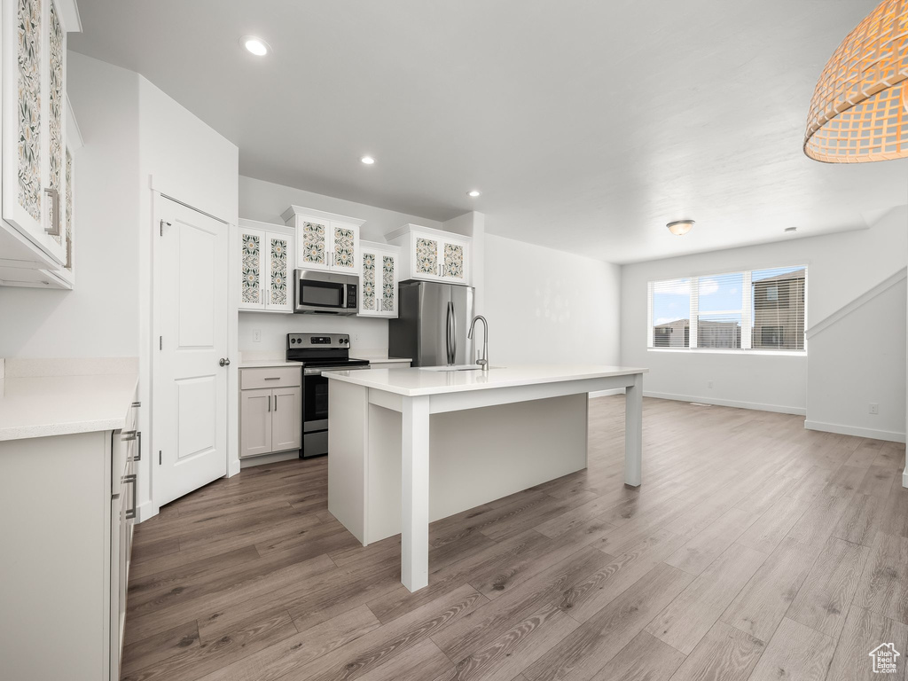 Kitchen featuring appliances with stainless steel finishes, light wood finished floors, a center island with sink, light countertops, and recessed lighting