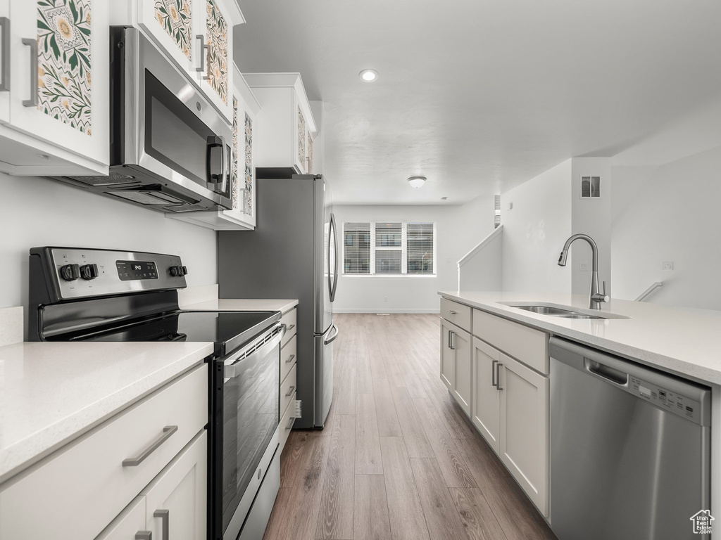 Kitchen with stainless steel appliances, white cabinetry, wood finished floors, light countertops, and recessed lighting