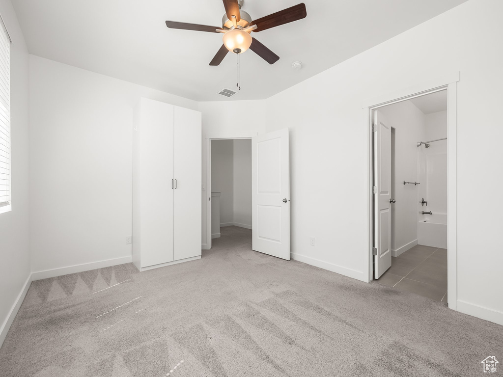 Unfurnished bedroom featuring light carpet, connected bathroom, and a ceiling fan