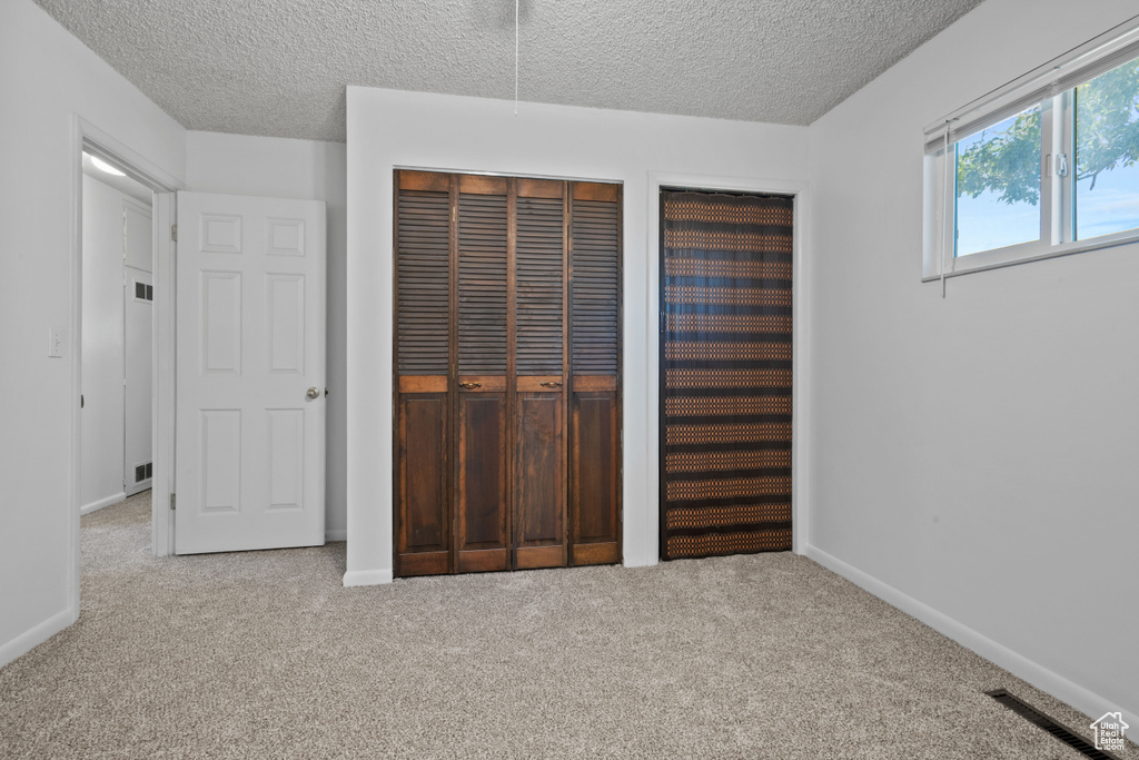 Unfurnished bedroom with carpet, a textured ceiling, and multiple closets