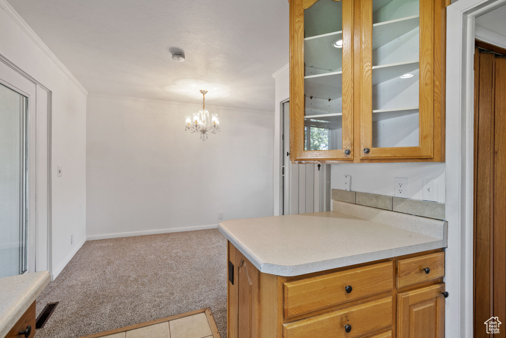 Kitchen featuring carpet, ornamental molding, a chandelier, light countertops, and glass insert cabinets