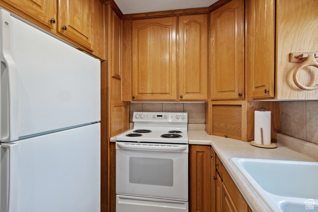 Kitchen with white appliances, backsplash, light countertops, and brown cabinetry