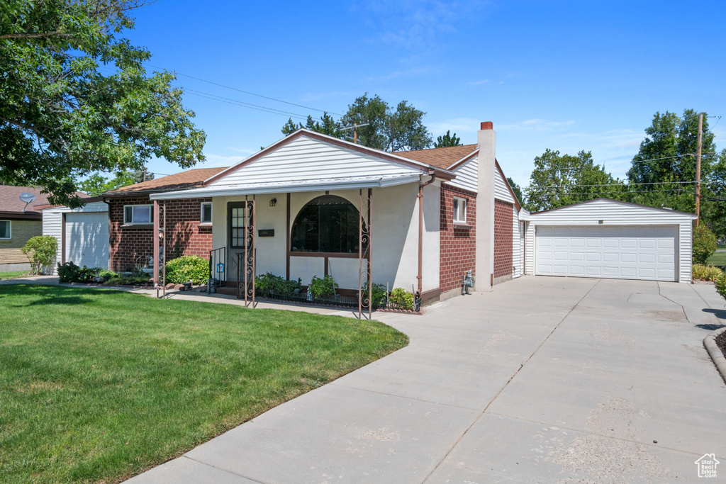 View of front of house featuring an outdoor structure, covered porch, a detached garage, a front lawn, and a chimney