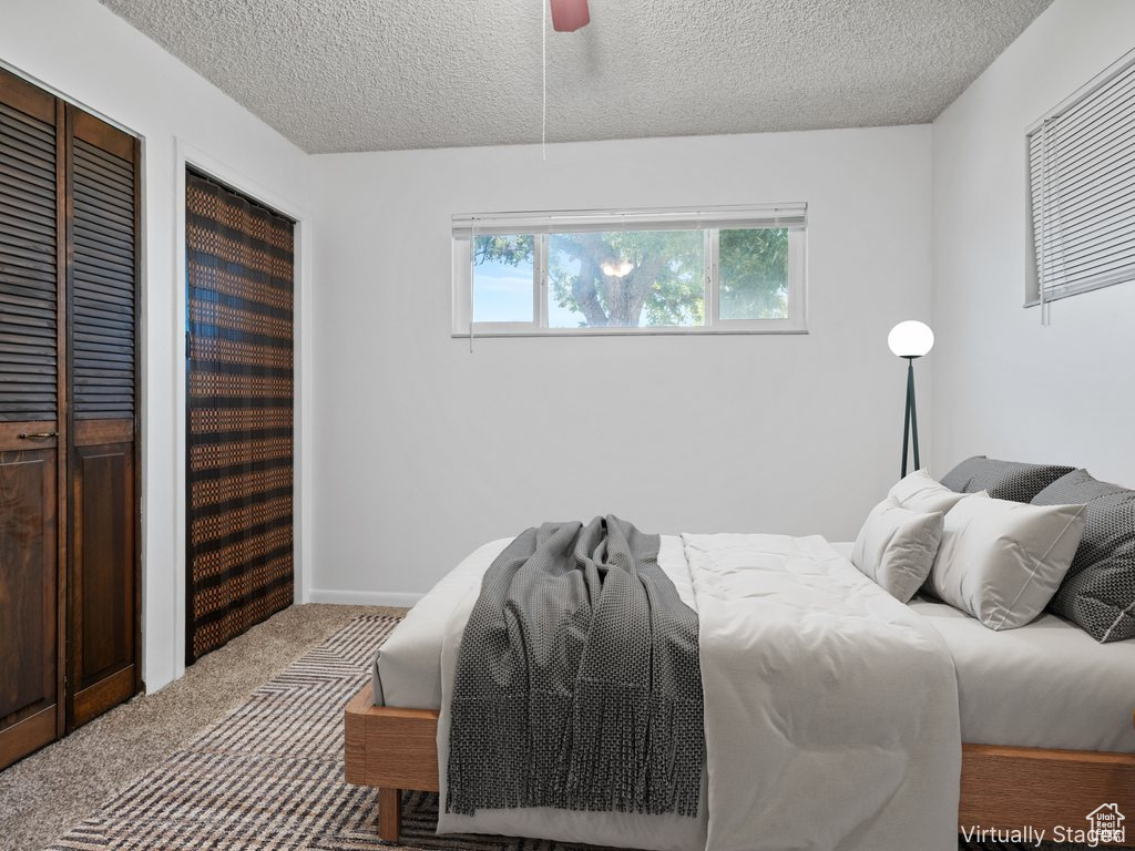 Carpeted bedroom featuring a textured ceiling, multiple closets, and ceiling fan