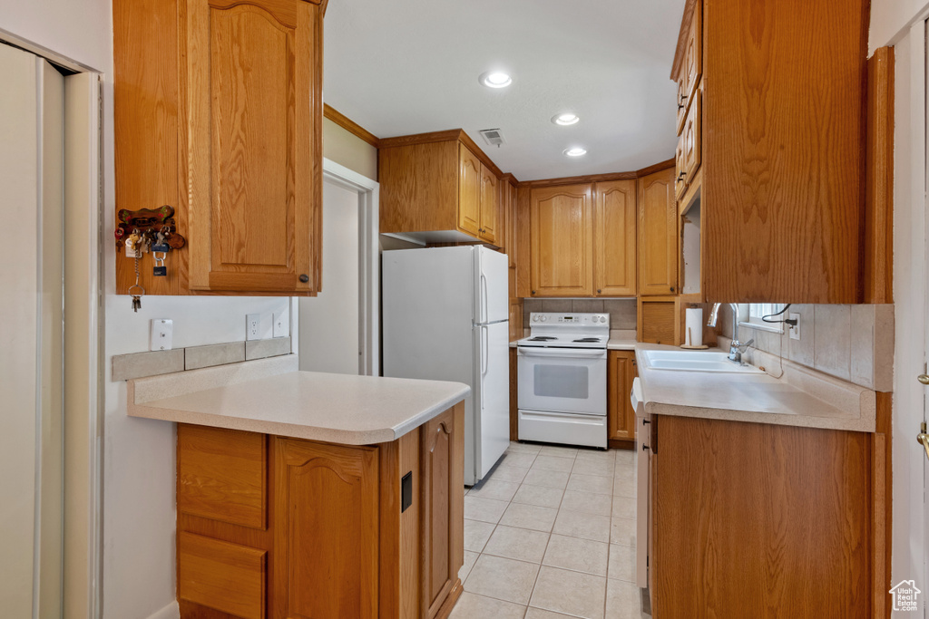 Kitchen with white appliances, light tile patterned floors, brown cabinets, light countertops, and a peninsula