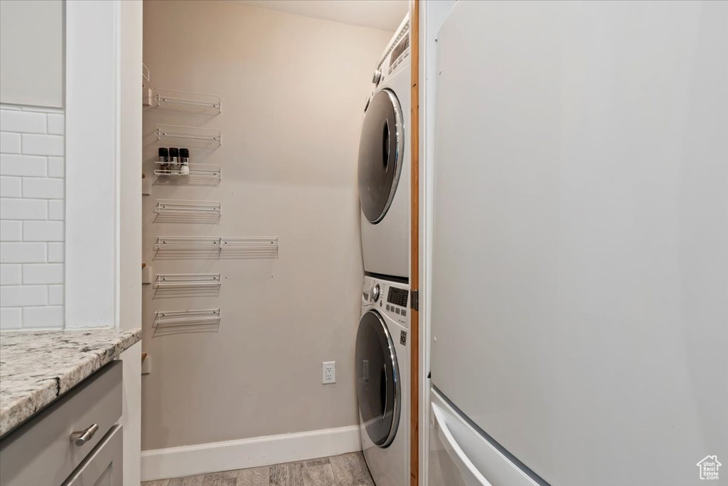 Washroom featuring stacked washer / drying machine, cabinet space, and light wood-style flooring