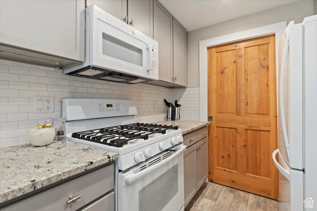 Kitchen with white appliances, gray cabinetry, light wood-type flooring, and decorative backsplash