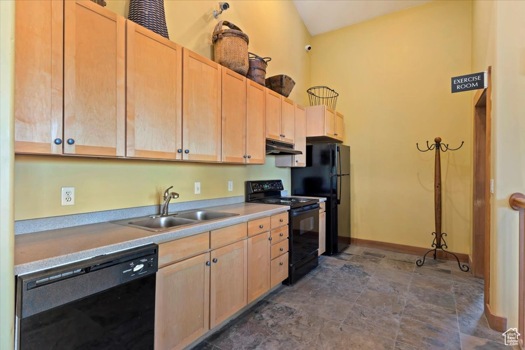 Kitchen featuring black appliances, under cabinet range hood, light brown cabinets, and vaulted ceiling