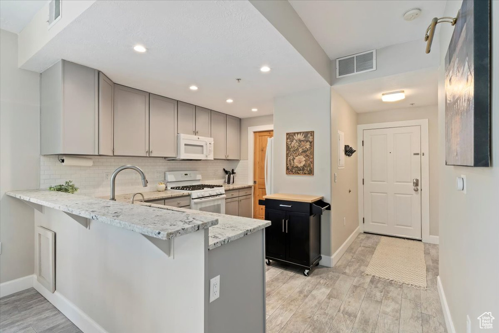 Kitchen featuring white appliances, light wood-style flooring, light stone countertops, backsplash, and recessed lighting