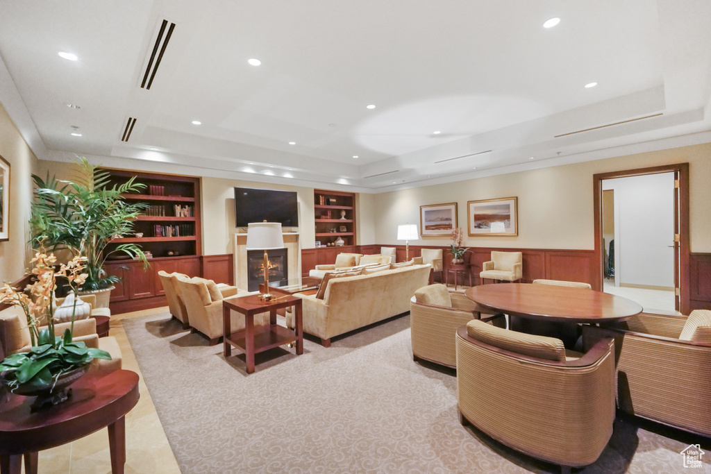 Living area featuring built in shelves, a tray ceiling, a glass covered fireplace, recessed lighting, and wainscoting